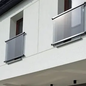 Französischer Balkon mit modernem Glasgeländer an weißer Hausfassade im Tageslicht.