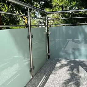 Moderner Balkon mit Edelstahlgeländer und satiniertem Glas als Sichtschutz im Sonnenlicht.
