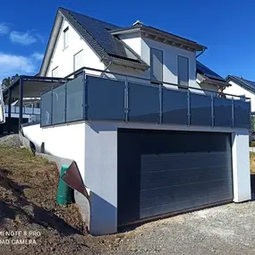 Modernes Einfamilienhaus mit Glasbalkon, großer Garage und Solaranlage auf dem Dach.
