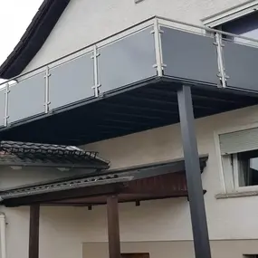 Moderner Balkon mit Glasgeländer und Metallstützen an einem Einfamilienhaus angebracht.