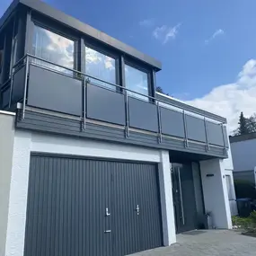 Modernes Einfamilienhaus mit großem Balkon und Doppelgarage, blauer Himmel im Hintergrund.