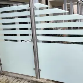 Moderner Sichtschutzzaun aus satiniertem Glas und Edelstahl vor einem Wohngebäude.