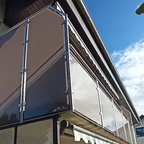 Moderner Balkon mit Sichtschutz und Glasverkleidung an einem Einfamilienhaus bei Sonnenschein.