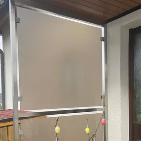 Sichtschutz aus mattem Glas auf Balkon mit Metallrahmen neben Haustür und Holzdach.
