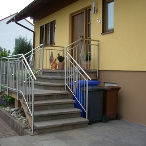 Eingangsbereich eines Hauses mit moderner Metalltreppe, Geländer und Mülltonnen.
