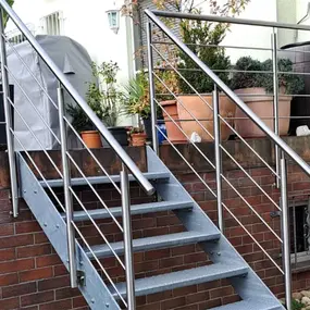 Stahl-Außentreppe mit Edelstahlgeländer und Pflanzkübeln auf einer Terrasse im Garten.