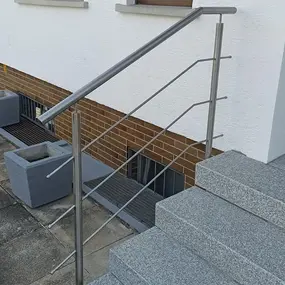 Modernes Edelstahlgeländer an einer Außentreppe mit Granitstufen und Pflanzkübeln.