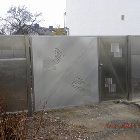 Modernes Edelstahl-Gartentor mit dekorativen Lochmustern vor einem Wohnhaus.