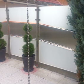 Moderner Sichtschutz auf Balkon mit Topfpflanzen, Ketten und blühenden Blumen.