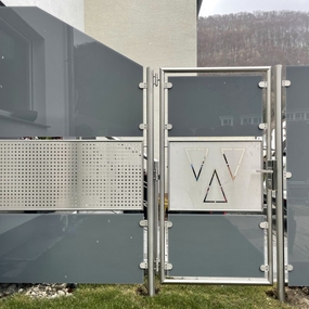 Moderner Sichtschutzzaun aus Glas und Edelstahl mit geometrischen Mustern im Vorgarten.