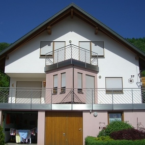 Modernes Einfamilienhaus mit Balkon, Garage und gepflegtem Garten bei sonnigem Wetter.