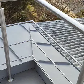 Flachdach mit Edelstahlgeländer und angrenzender Wellblechdachfläche im Außenbereich.